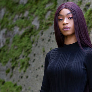 A Bradford student standing in front of a grey slate wall with moss on it