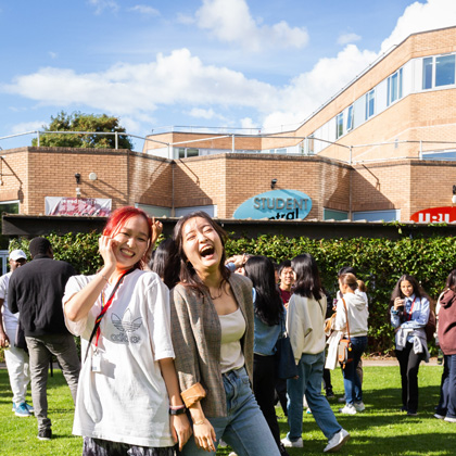 Two students smiling on the amphitheatre outside of Student Central, which is busy with students.