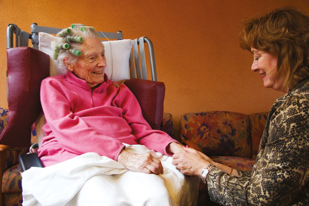 An elderly lady holding hands with a visitor.
