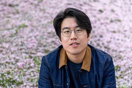 Dong Kim, a student sat on a wall with blossom in the background
