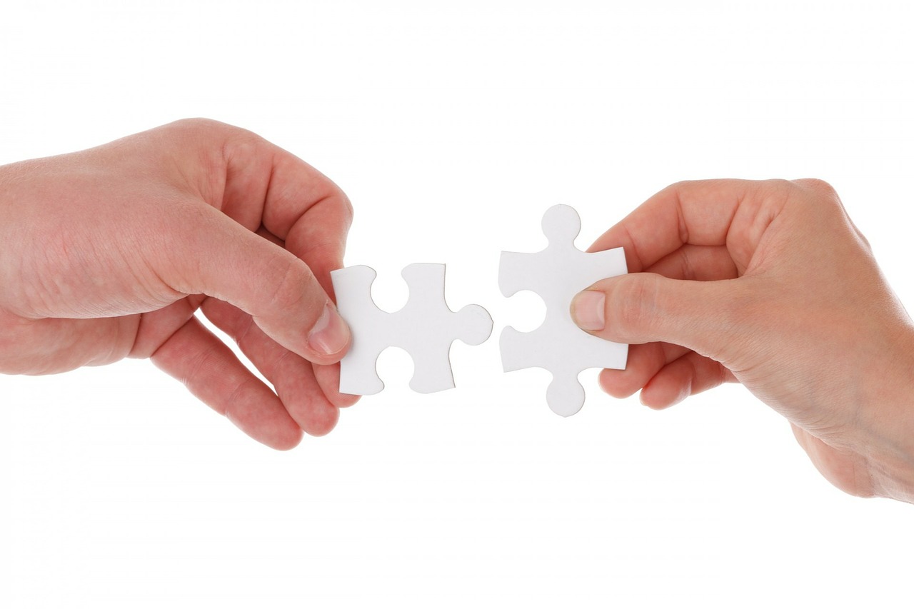 Hands fitting jigsaw pieces together representing teamwork.