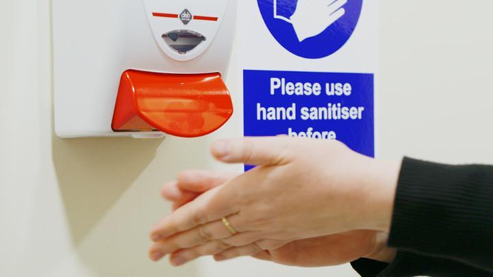 A person dispensing hand sanitiser from a wall mounted unit