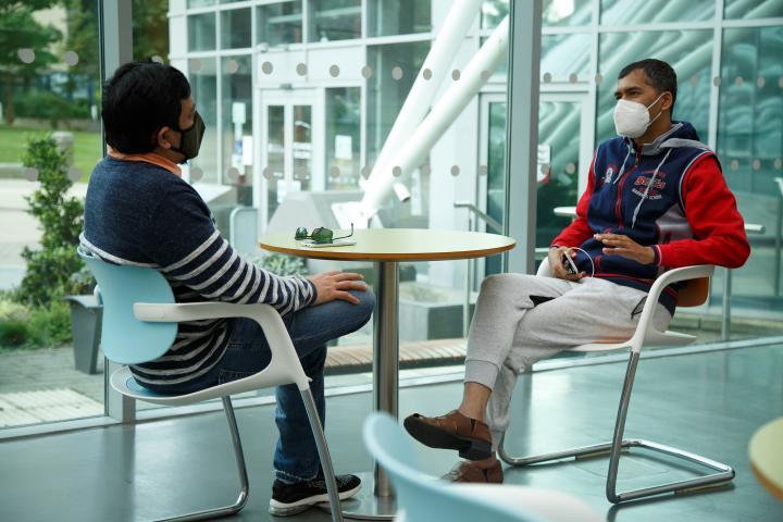 Two students wearing face masks are seated at a table in the Richmond building atrium