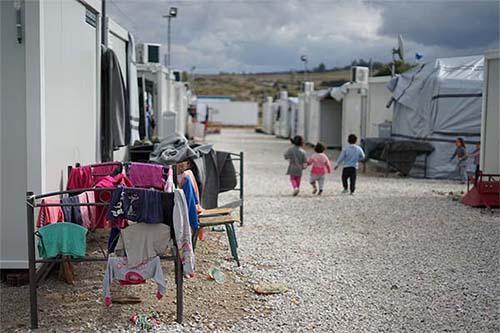Children walking down a street with makeshift housing and no facilities 