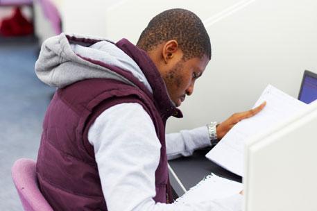 A male postgraduate student sitting at a desk working with papers and a computer