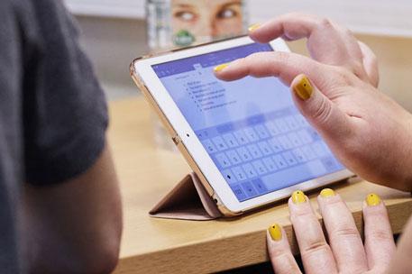 A student's hands using an iPad, resting on a desk.