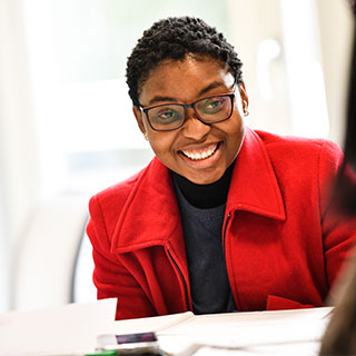 Student in red coat, smiling at something behind the camera.