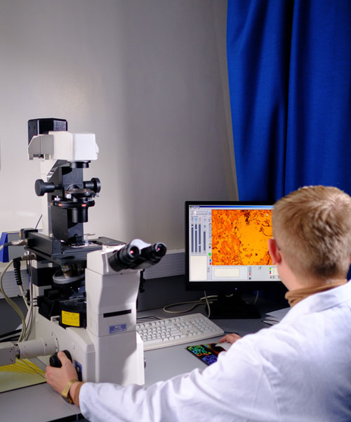 A student in a white coat working at a computer with lab equipment