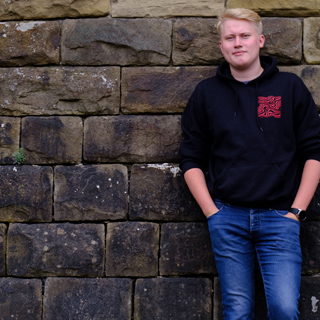 Stephen, Computer Science for Cyber Security student stood in front of a stone wall 
